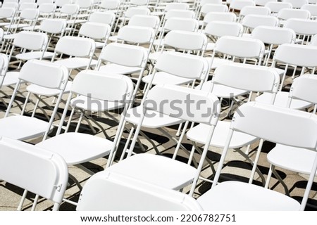 White plastic chairs for a concert, wedding or business conference stand in rows on the street. Folding chairs stand in a row for a public event in the city.