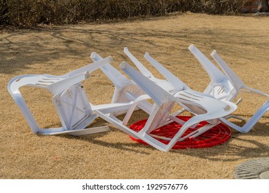 White Plastic Chairs Turned Over On Top Of Red Plastic Table.