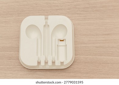 A white plastic container for storing wired headphones. On a wooden background.