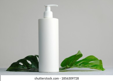White plastic cosmetics container for cream or shampoo. Cosmetics bottle mockup with tropical leaves. Beauty product packaging, skincare and haircare concept.