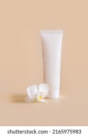 White plastic cream tube near white orchid flower on light yellow, close up, mockup. Skincare beauty product, cream or lotion. Exotic natural cosmetics, pastel minimal composition