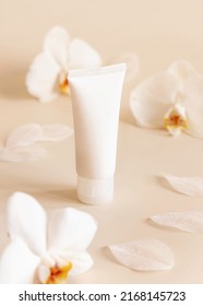 White plastic cream tube near white orchid flowers on light yellow, close up, mockup. Skincare beauty product, cream or lotion. Exotic natural cosmetics, pastel minimal composition
