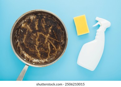 White plastic detergent spray bottle, yellow cleaning sponge and stainless frying pan with burn grease stain on light blue table background. Pastel color. Closeup. Washing dirty pan. Top view. - Powered by Shutterstock