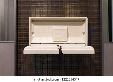 White Plastic Diaper Table On Brown Ceramic Wall In Toilet. Baby Diaper Table In A Public Restroom