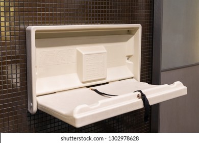 White Plastic Diaper Table On Brown Ceramic Wall In Toilet. Baby Diaper Table In A Public Restroom