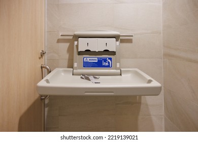 White Plastic Diaper Table On Marble Tile Wall In Toilet. Baby Changing Station In A Public Restroom.