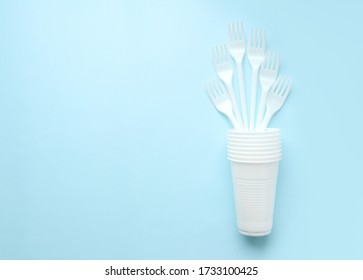 White plastic disposable forks stand in a stack of white glasses on a blue background. Space for text. Selective focus. Copy space