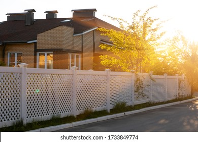 White plastic fence around a typical house in a cottage village. Concept of landscaping, protection, fencing of a territory.