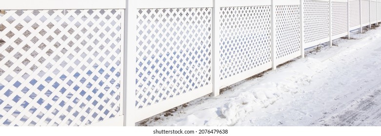 White Plastic Fence In A Modern Cottage Village On A Clear Winter Day. Snow Drifts In Front Of A Vinyl Fence. Banner