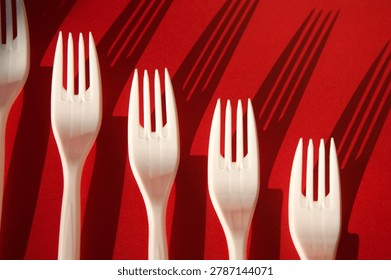 White Plastic Forks Casting Shadows on Red Background 