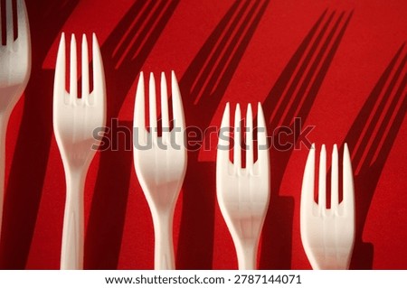 White Plastic Forks Casting Shadows on Red Background 