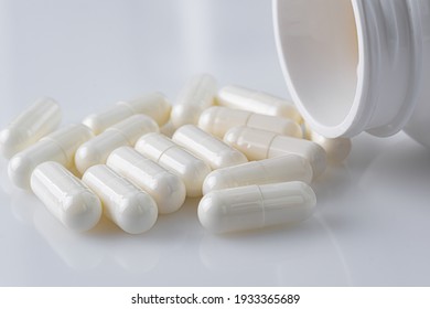 white plastic medicine vial can bottle with white capsules on white background, with a blur