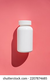 White Plastic Pills Bottle, Vitamins Or Food Supplemets. Container With Medication Pills On Pink Background With Sun Light And Shadows