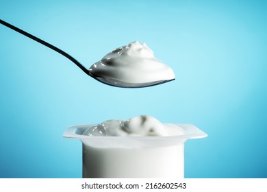 White Plastic Pot With Yogurt And Spoon On Blue Background