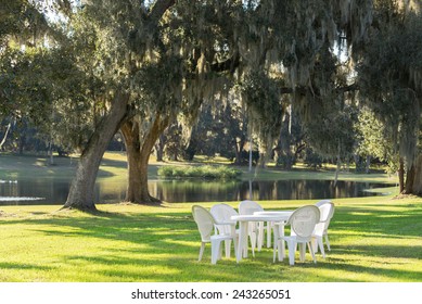 White Plastic Table And Chairs Outside In A Garden On Green Lawn By A Pond Or Lake In The Afternoon Sun And A Peaceful Relaxing Serene Tranquil Setting