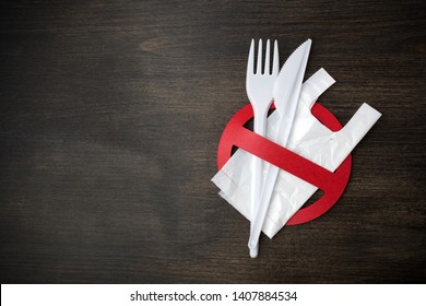 White plastic tableware on a wooden background as a symbol of environmental pollution. Ban single use plastic.