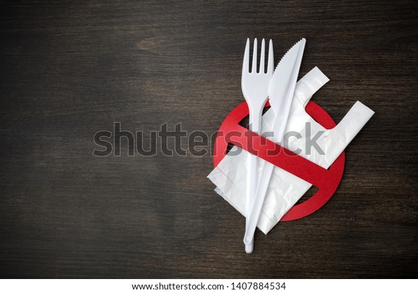 White\
plastic tableware on a wooden background as a symbol of\
environmental pollution. Ban single use\
plastic.