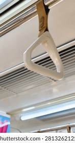 ​Close-up of a white plastic triangular hand strap hanging from a metal rod inside a commuter train.