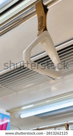 ​Close-up of a white plastic triangular hand strap hanging from a metal rod inside a commuter train.