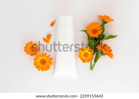 White plastic tube with face, hand and body cream and calendula,marigold flowers. Organic cosmetic concept,template . Flat lay,copy space.