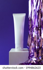 White Plastic Tube Mockup With Moisturizer Cream, Shampoo Or Facial Cleanser And Holiday Tinsel On Cube Podium On Violet Background, Vertical