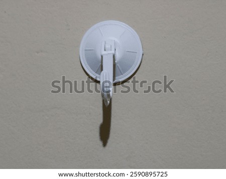 White plastic wall hook featuring a suction attachment, perfect for holding items against walls. Designed for home organization, it is convenient and easy to use for various purposes.