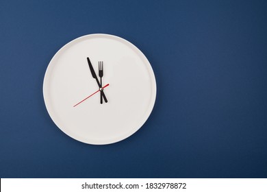 White Plate Clock On A Blue Background With Copy Space. The Hands Point To 12 O'clock. Interval Fasting Or Autophagy.