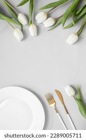 white plate and cutlery, tulips on a pastel grey background. copy space