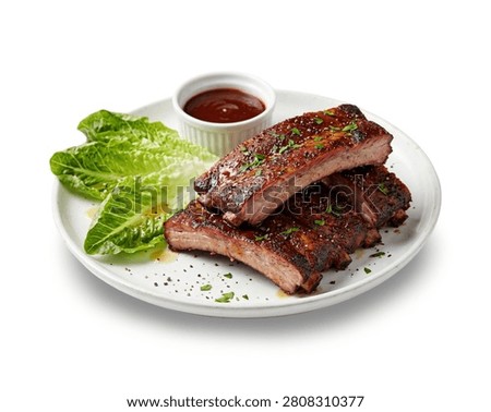 A white plate featuring a stack of grilled barbecue ribs coated in sticky sauce and topped with green onions, served alongside a fresh garden salad with lettuce, tomatoes, and red onions, isolated on a white background 