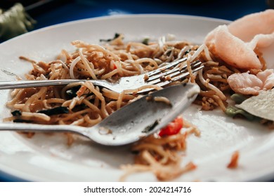 A white plate filled with leftover fried noodles, typical of traditional Indonesian food.