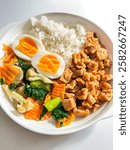 a white plate filled with a simple and hearty meal. A mound of white rice sits in the center, surrounded by stir-fried vegetables, tofu, and two halved hard-boiled eggs