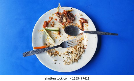 White Plate And Fork With Leftover Food On The Blue Table After Dinner