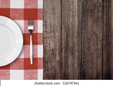 white plate and fork on old wooden table with red checked tablecloth and copyspace