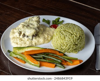 A white plate with a grilled chicken breast topped with a rich, creamy sauce, served alongside a colorful assortment of roasted vegetables - Powered by Shutterstock