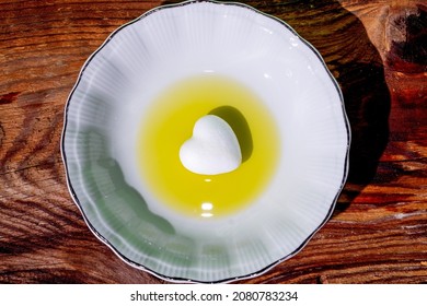 White plate. A little white heart in oil on a plate. Harsh shadow. Wood background. Top view. Cooking, health, fresh, organic, concept. Minimal style.