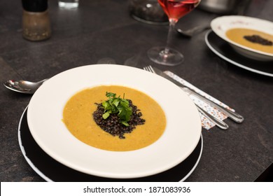 White Plate On Dark Table With Chick Pea Soup Topped With Black Lentils And Fresh Coriander