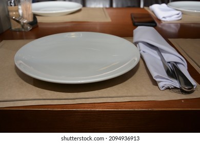 A White Plate On A Paper Napkin And A Knife With A Fork Wrapped In A White Cloth Napkin In A Beer Restaurant Before Eating Meat Dishes For Beer