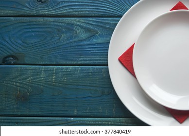 White Plate With Red Napkin On A Blue Wooden Board. Serving Dishes And Cutlery