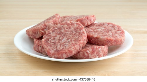 A White Plate With Sausage Patties Atop A Wood Counter Top.