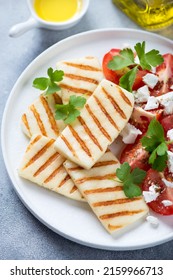 White plate with slices of grilled halloumi cheese, tomatoes and fresh parsley, vertical shot, selective focus, close-up