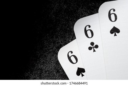 white playing cards 666 six of spades and six of clubs in the right lower corner on black cast iron surface with copy space at the left side, three of a kind, triple six
