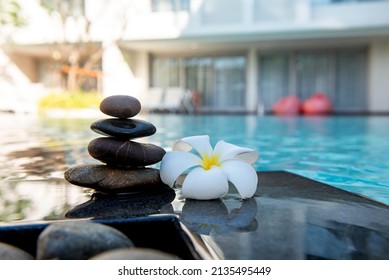 White Plumeria or frangipani flower and stone stack standing beside the swimming pool with reflection. Blurred background.