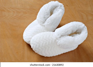 White Plush Slippers On Hardwood Floor.  Concept - Comfort And Relaxation