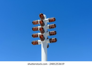 A white pole with multiple red-caged lights stands against a clear blue sky