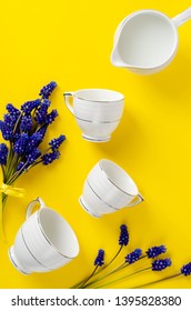 White Porcelain Coffe Or Tea Set, Jar With Milk, Muscari Flowers On Yellow Background. Top Down. Flat Lay. Vertical Composition. Crockery Concept