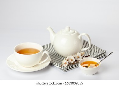 White porcelain cup of tea, teapot and honey on a table. Close-up side view of a porcelain tea set on a white background.