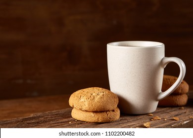White porcelain mug of tea and sweet cookies on piece of wood over wooden background, top view, selective focus