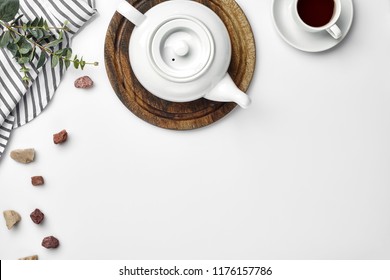 A white porcelain teapot on a wooden board and a white cup with tea on a table. Top view. Copy space.