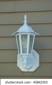 A White Porch Light Against A Brown Vinal Siding