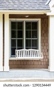 White Porch Swing In Front Of Window And Between Columns Of A Brown Shingled House - Vertical